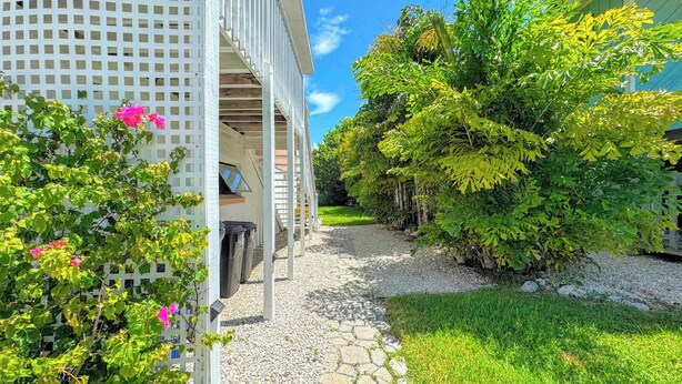 A pathway leading to a building with a covered porch and a garden area with trees and shrubs.