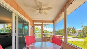 A covered outdoor area with a round table and red chairs, a ceiling fan, and a view of a residential area. - 231 Dundee Cozy Home Short Walk to Beach (Fort Myers Beach)