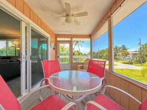 A covered outdoor area with a round table and red chairs, a ceiling fan, and a view of a residential area. - 231 Dundee Cozy Home Short Walk to Beach (Fort Myers Beach)