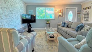 A living room with a television, two sofas, a coffee table, and a window with blinds.