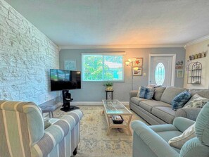 Una sala de estar con televisor, dos sofás, una mesa de centro y una ventana con persianas.