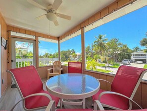 A room with a glass table and red chairs, a ceiling fan, and a view of a residential street with palm trees. - 231 Dundee Cozy Home Short Walk to Beach (Fort Myers Beach)