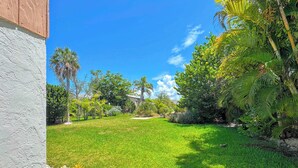 A well-maintained lawn with a variety of trees and shrubs, a clear blue sky, and a building in the background.