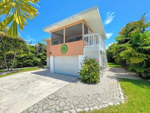A two-story house with a garage, surrounded by a well-maintained garden and palm trees. - 231 Dundee Cozy Home Short Walk to Beach (Fort Myers Beach)