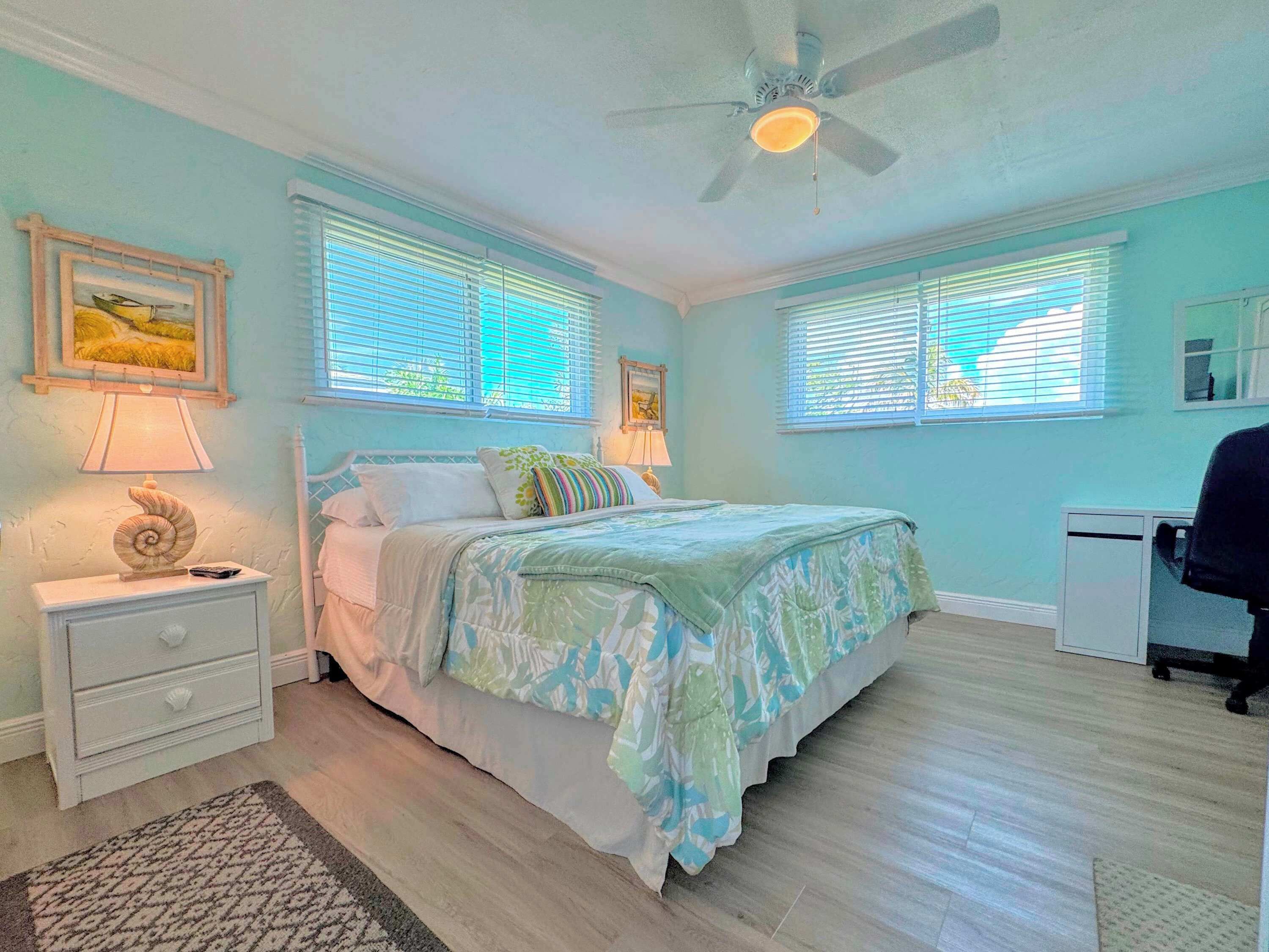 A bedroom with a bed, nightstands, a desk, and a ceiling fan.