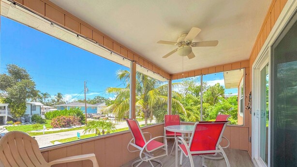 A balcony with a table and chairs, a ceiling fan, and a view of a residential area with houses and greenery. - 231 Dundee Cozy Home Short Walk to Beach (Fort Myers Beach)