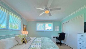 A bedroom with a bed, a desk, a chair, and a ceiling fan.