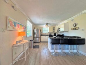 A kitchen with a refrigerator, microwave, and bar stools. - 231 Dundee Cozy Home Short Walk to Beach (Fort Myers Beach)