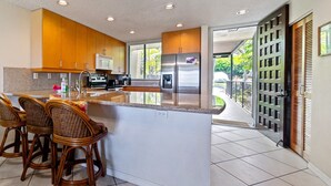 Una cocina moderna con una isla grande, taburetes de bar, electrodomésticos de acero inoxidable y vistas al exterior.