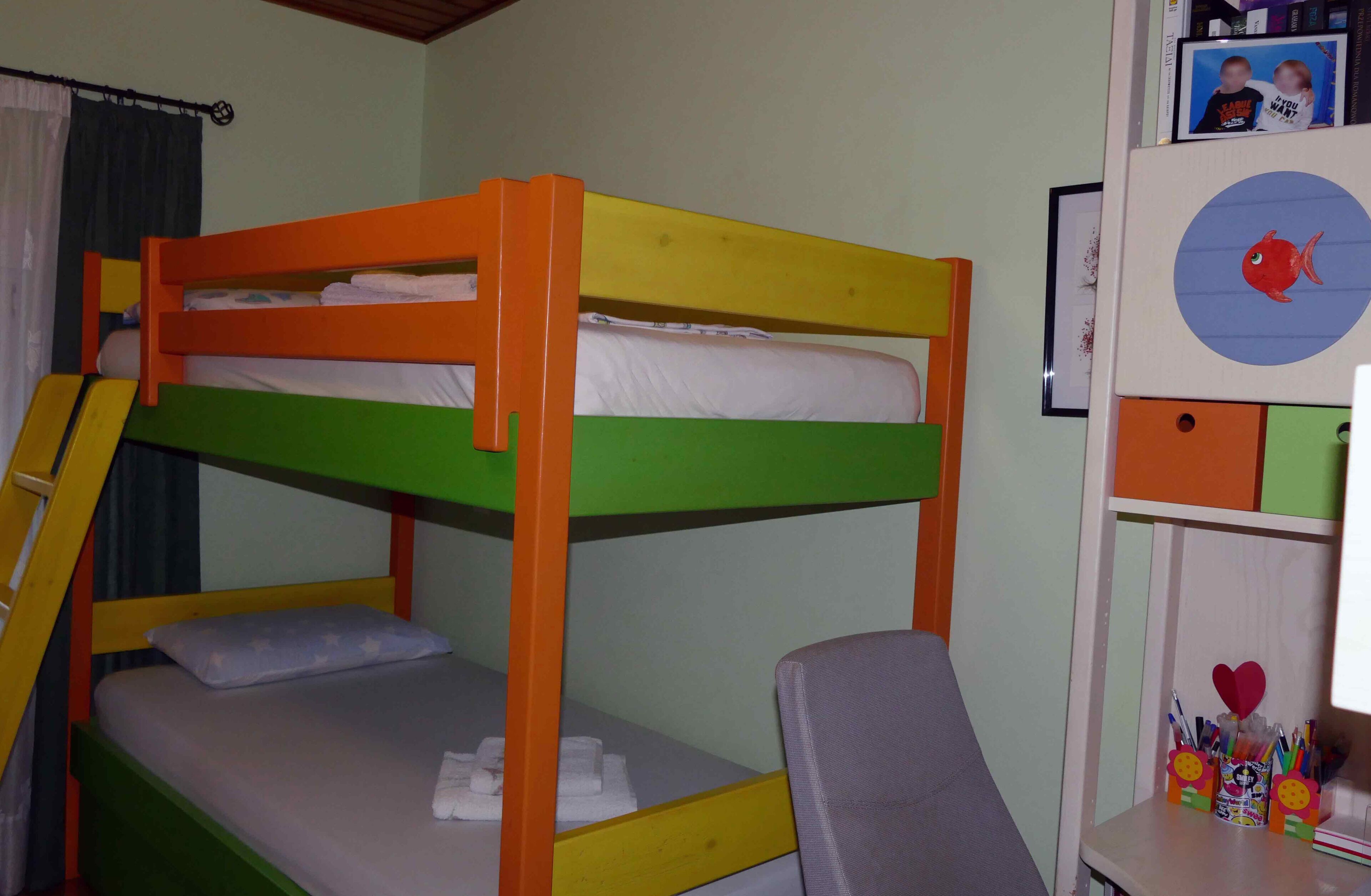 A bunk bed with a ladder, a desk with a chair, and a shelf with storage boxes and pens.