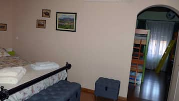 Un dormitorio con una cama, un taburete pequeño y una cama litera al fondo.