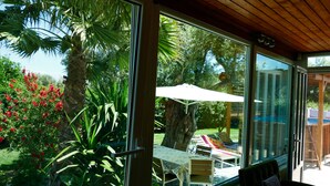 A room with large windows, a wooden ceiling, and a view of an outdoor patio with a table and chairs. - esperides holidays (Marathon)