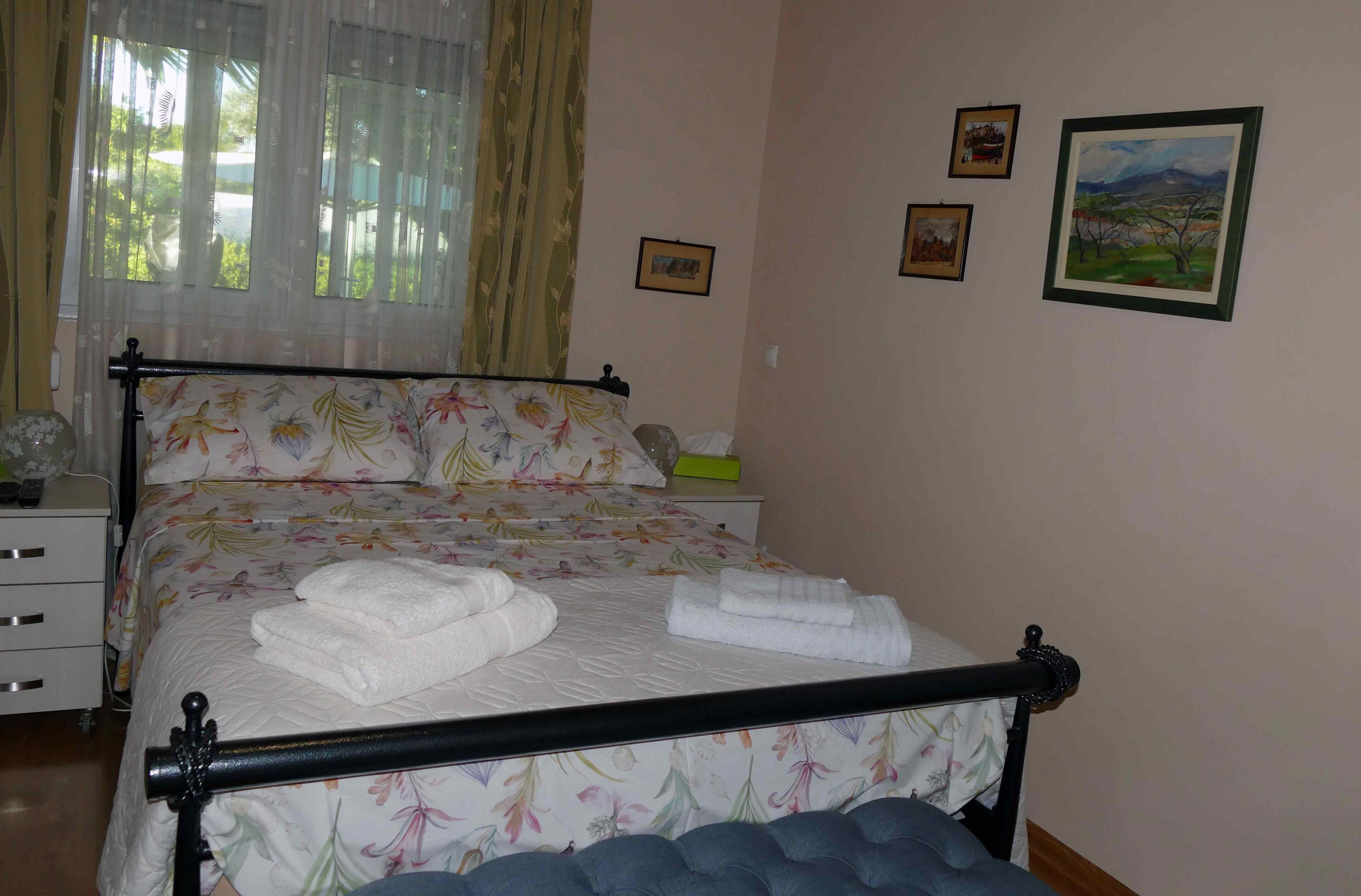 A neatly made bed with floral bedding, a bedside table with a lamp, and a window with curtains.
