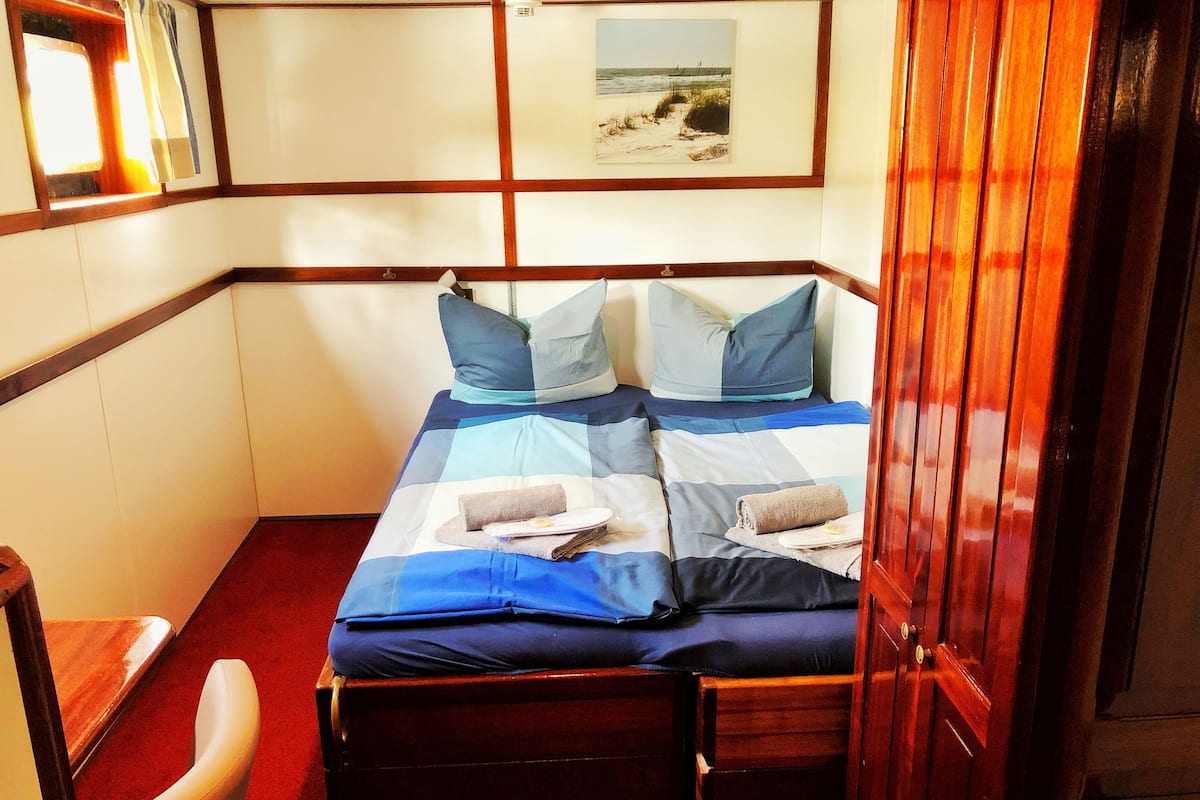 A small, compact room with a bed, a chair, and a window.