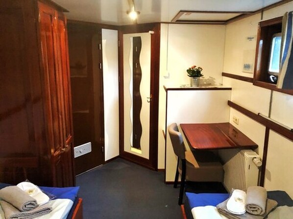 A compact room with a bed, a small table, and a chair. There is a radiator and a mirror on the wall.