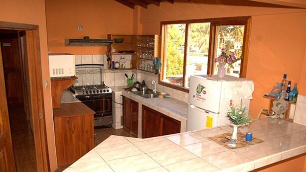 A compact kitchen with a stove, sink, and refrigerator. - Hostal La Isla del Descanso (Puerto Villamil)