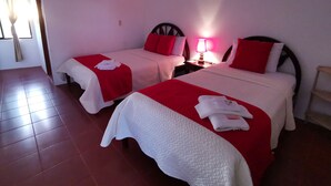 A hotel room with two beds, each with red and white bedding, a bedside lamp, and a painting on the wall. - Hostal La Isla del Descanso (Puerto Villamil)