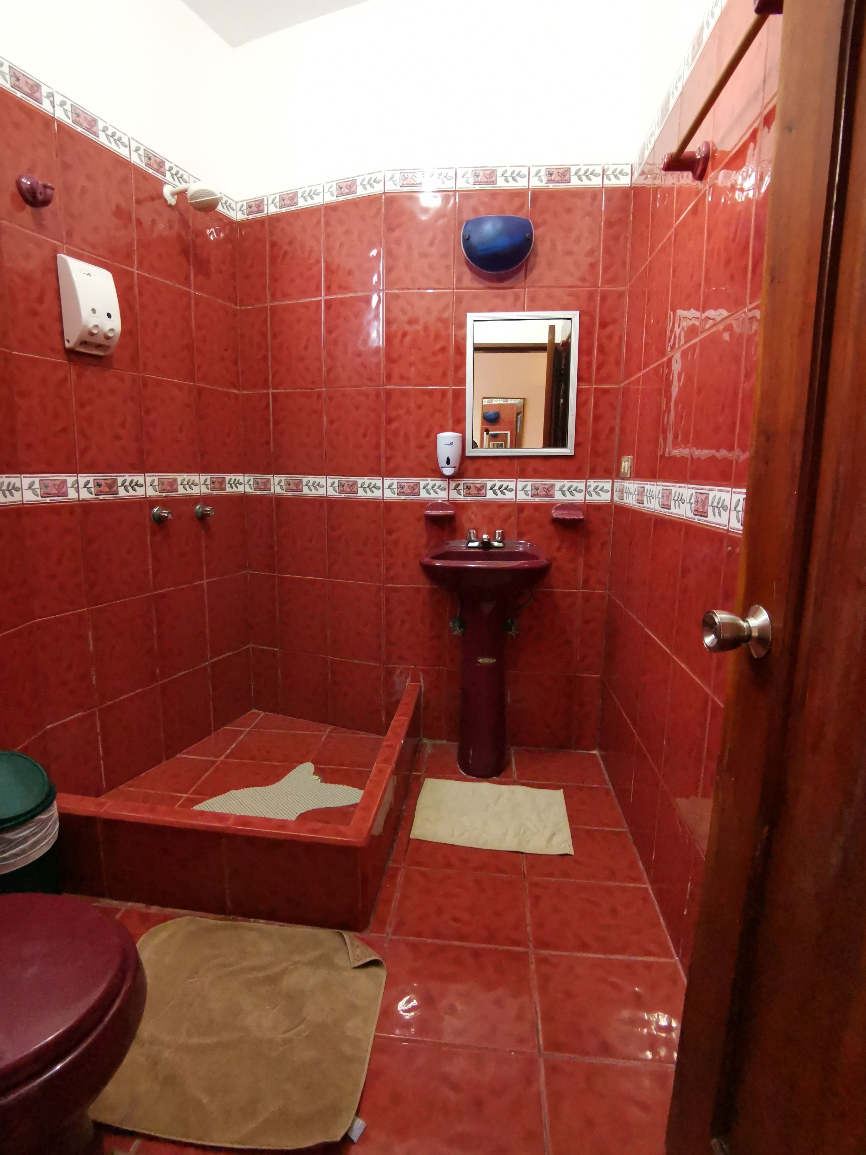 Ein Badezimmer mit roten Fliesenwänden, einem Waschbecken, einem Spiegel und einer Toilette.