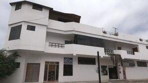 A multi-story white building with a flat roof, large windows, and a visible storefront. - Hostal La Isla del Descanso (Puerto Villamil)
