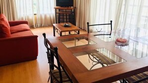 A modern living room with a glass-top dining table, a red sofa, and a flat-screen TV on a stand. - Tempo Light (Santiago)