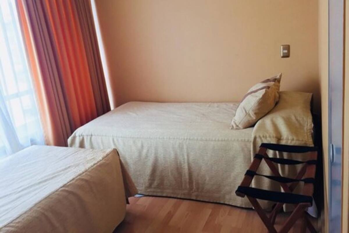 A small, single-bed room with a wooden floor and a window with curtains.