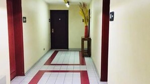 A hallway with white tiled floors and red borders, doors on both sides, and a black door at the end. - Tempo Light (Santiago)