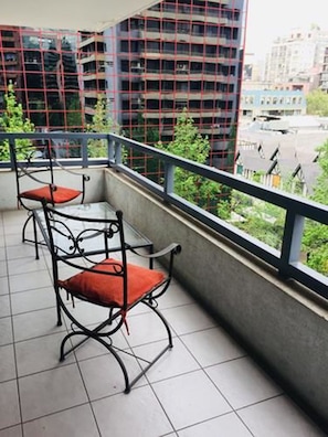 Un balcón con sillas y una mesa de metal, con vistas a un paisaje urbano lleno de edificios.