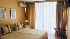 A hotel room with a large bed, a bedside table with a lamp, a chair, and a TV. - Tempo Light (Santiago)