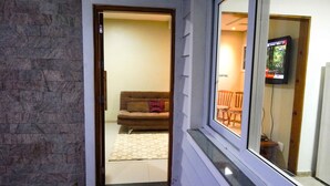 Un pasillo con pared de piedra y una puerta de madera que da a una sala de estar con sofá y televisor.