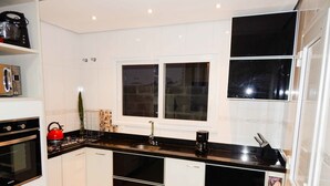 Una cocina moderna con armarios blancos, encimera negra, una mesa de comedor de madera y una ventana sobre el fregadero.