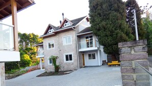 Una casa de dos pisos con entrada pavimentada, un muro de piedra y un árbol grande.
