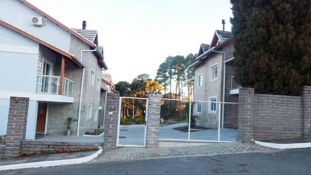 Una calle residencial con dos casas, un acceso con reja y un muro de piedra.
