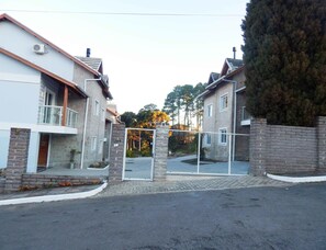 A residential street with two houses, a gated entrance, and a stone wall. - Residencial Villa Mariana (Gramado)