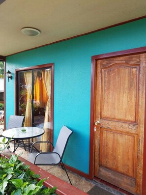 A room with a wooden door, a glass door with curtains, a round table with chairs, and a small potted plant. - Hostal Akapu (Hanga Roa)