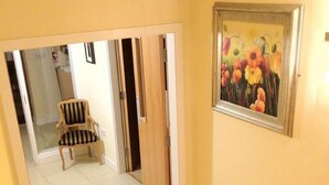Un couloir avec une chaise en bois, un tableau et une porte donnant sur une autre pièce.