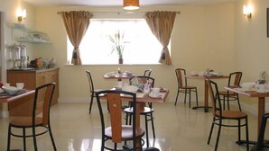 Un espace repas comprenant plusieurs tables et chaises, une fenêtre avec des rideaux et un luminaire au plafond.