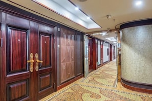A hallway with wooden doors, a patterned carpet, and a curved wall.
