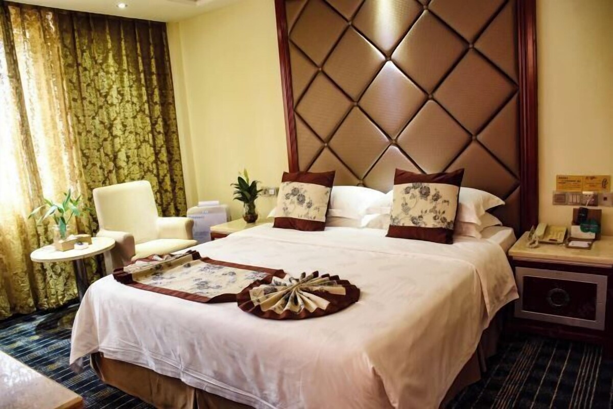 A hotel room with a large bed, a chair, a small table, and a decorative pillow arrangement.