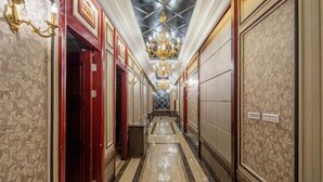 Un pasillo de hotel con paredes decoradas, una lámpara de araña y suelo de baldosas.