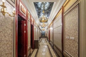 Un couloir d’hôtel aux murs décorés de motifs, orné d’un lustre et doté d’un sol carrelé.
