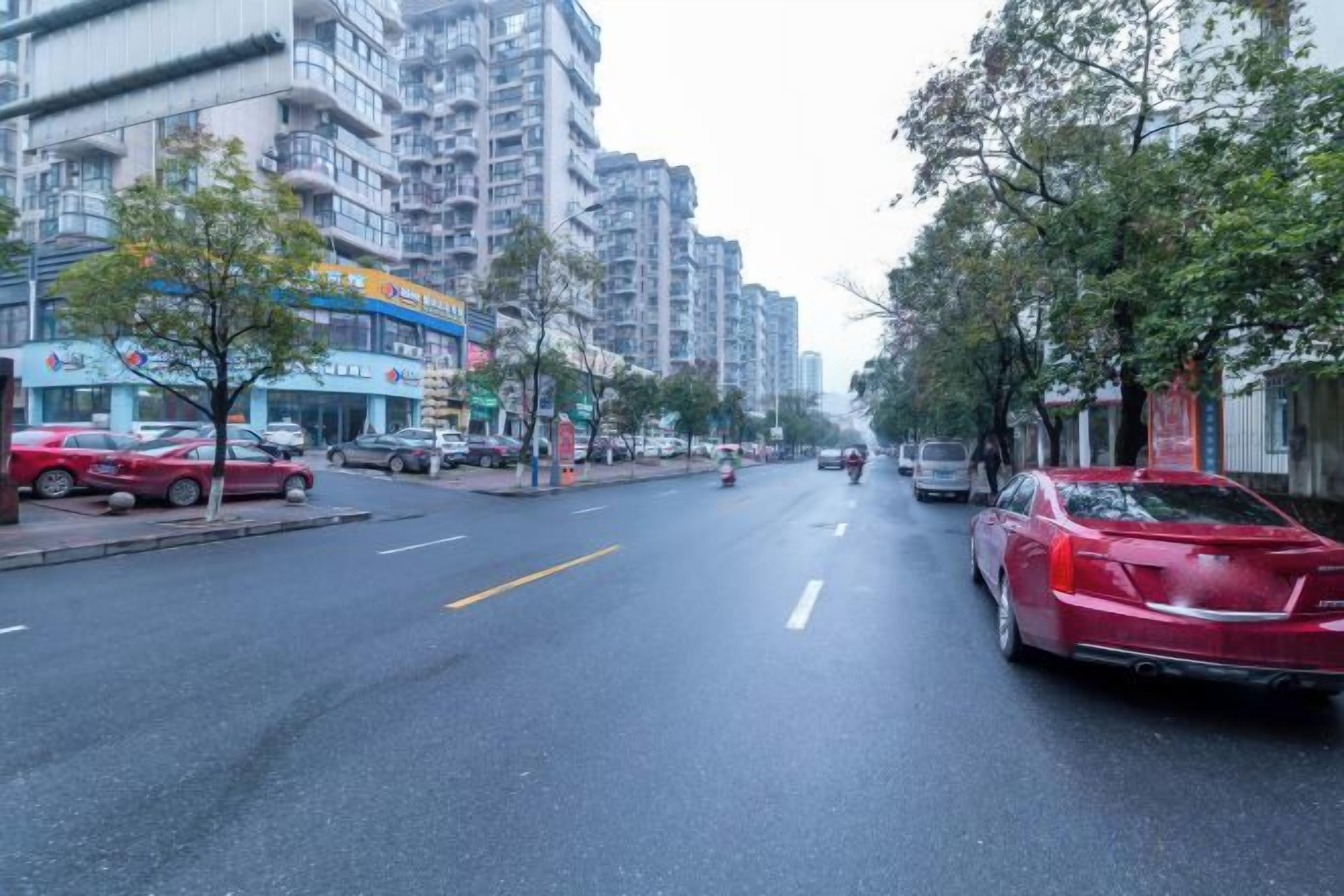 Una calle urbana con edificios, coches aparcados y árboles.