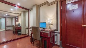 A hotel room with a wooden desk, a computer, a chair, a mirror, and a door with a sign.