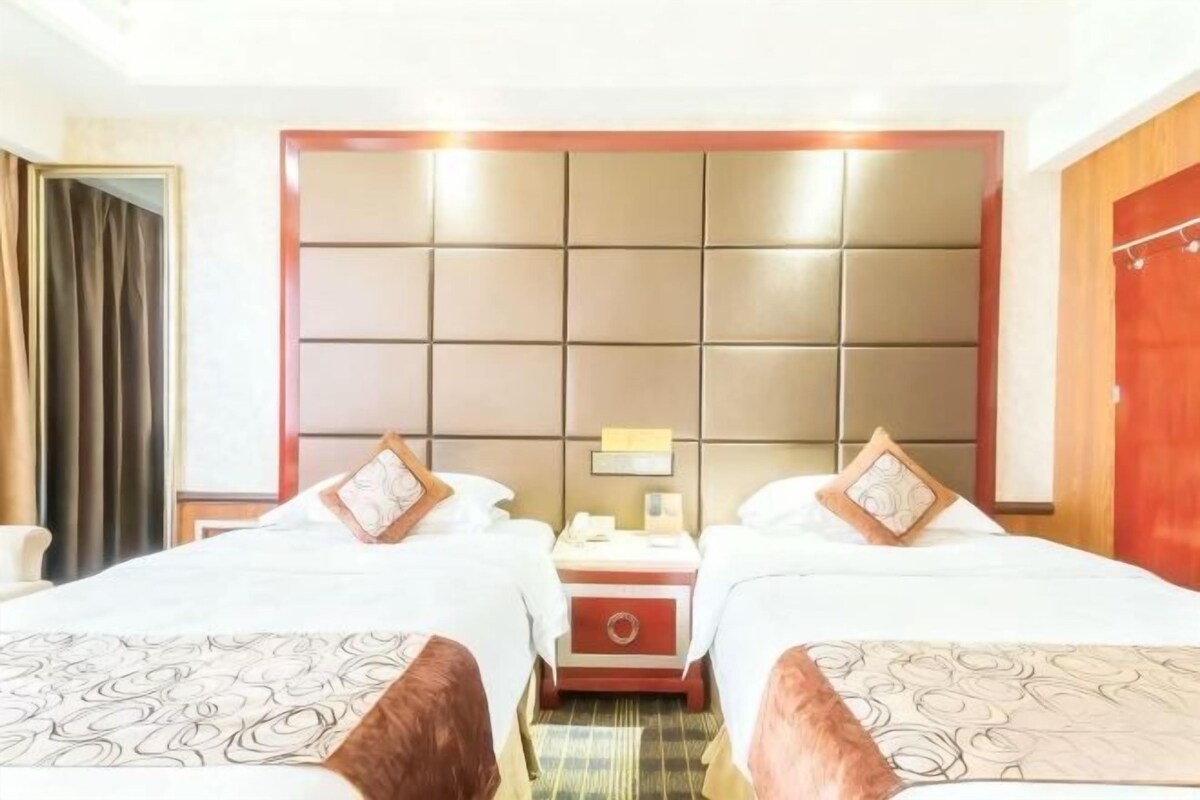 A hotel room with two beds, a headboard, a nightstand, and a mirror.