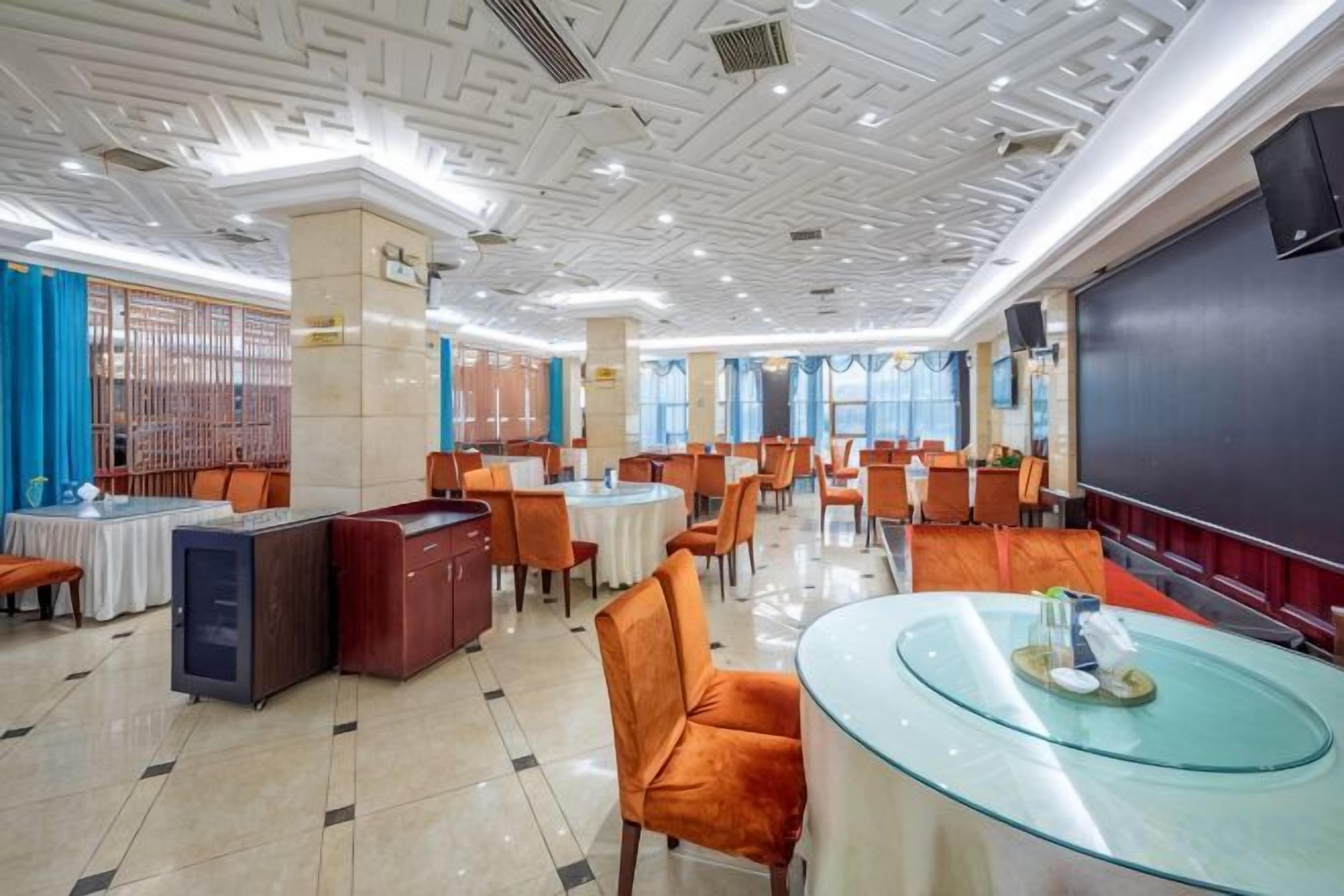 Un espace de restauration d’hôtel avec des tables rondes, des chaises orange et une table à plateau en verre.