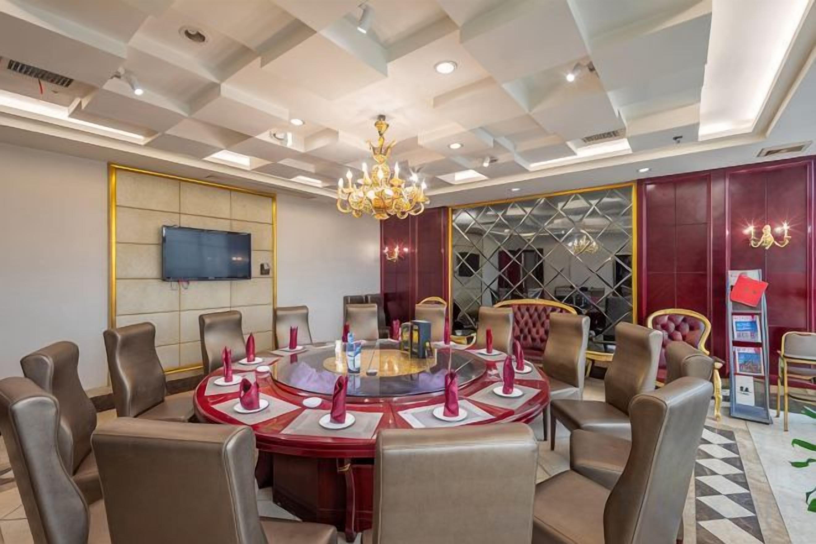 A conference room with a round table, chairs, a chandelier, and a television on the wall.