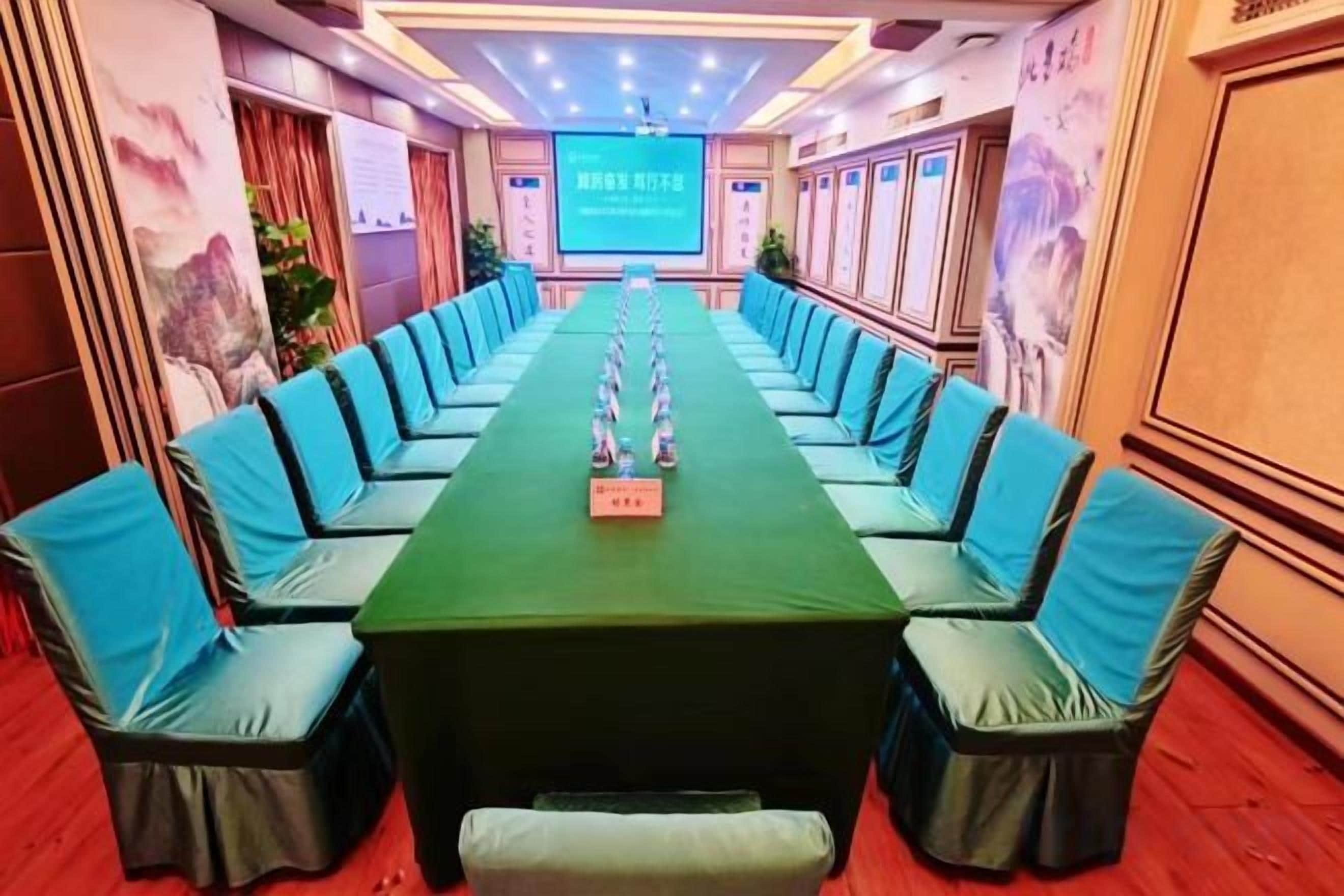 A conference room with a long table and chairs, a podium, and a screen at the front.