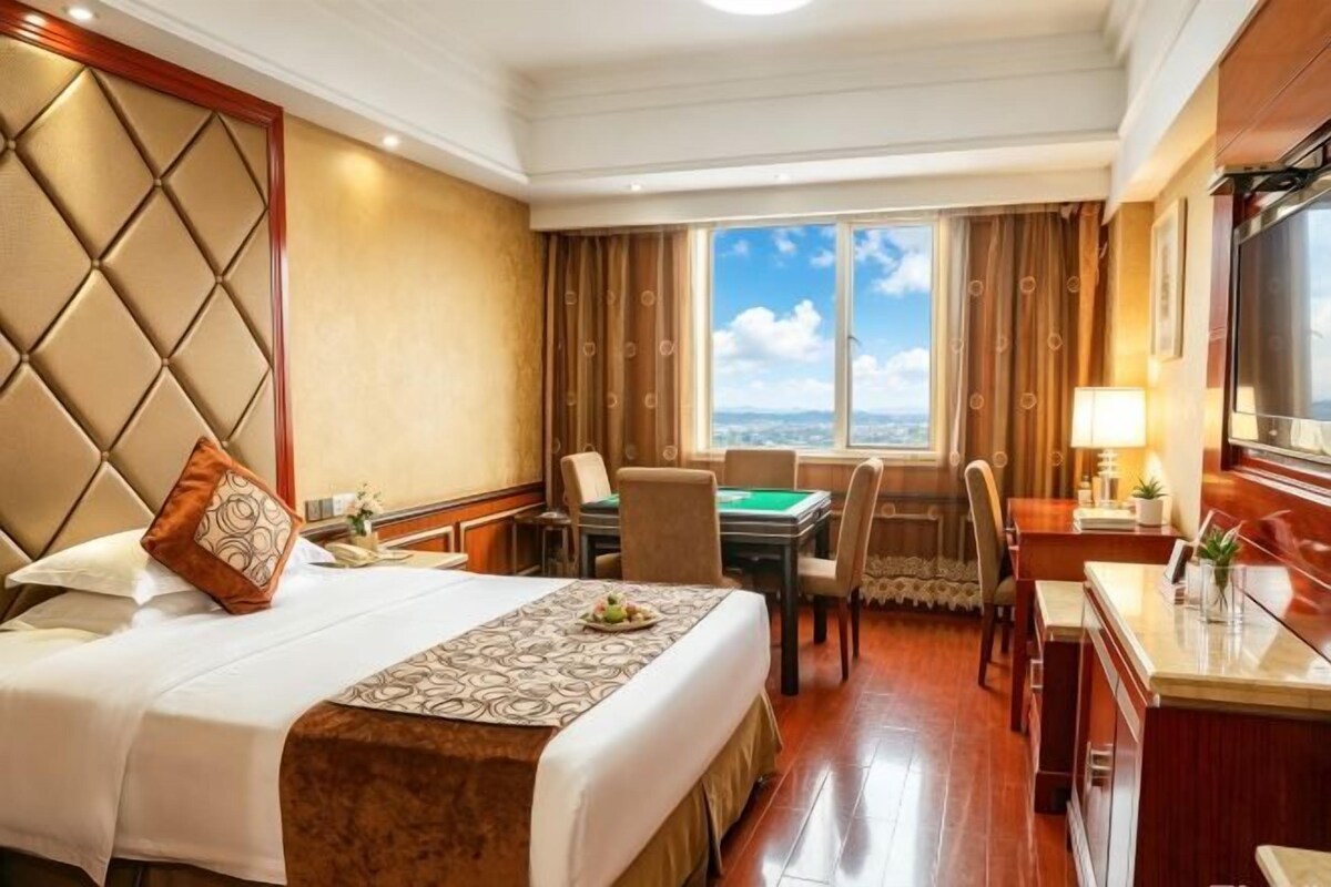 A hotel room with a bed, a desk, a chair, a dining table, and a view of the city.