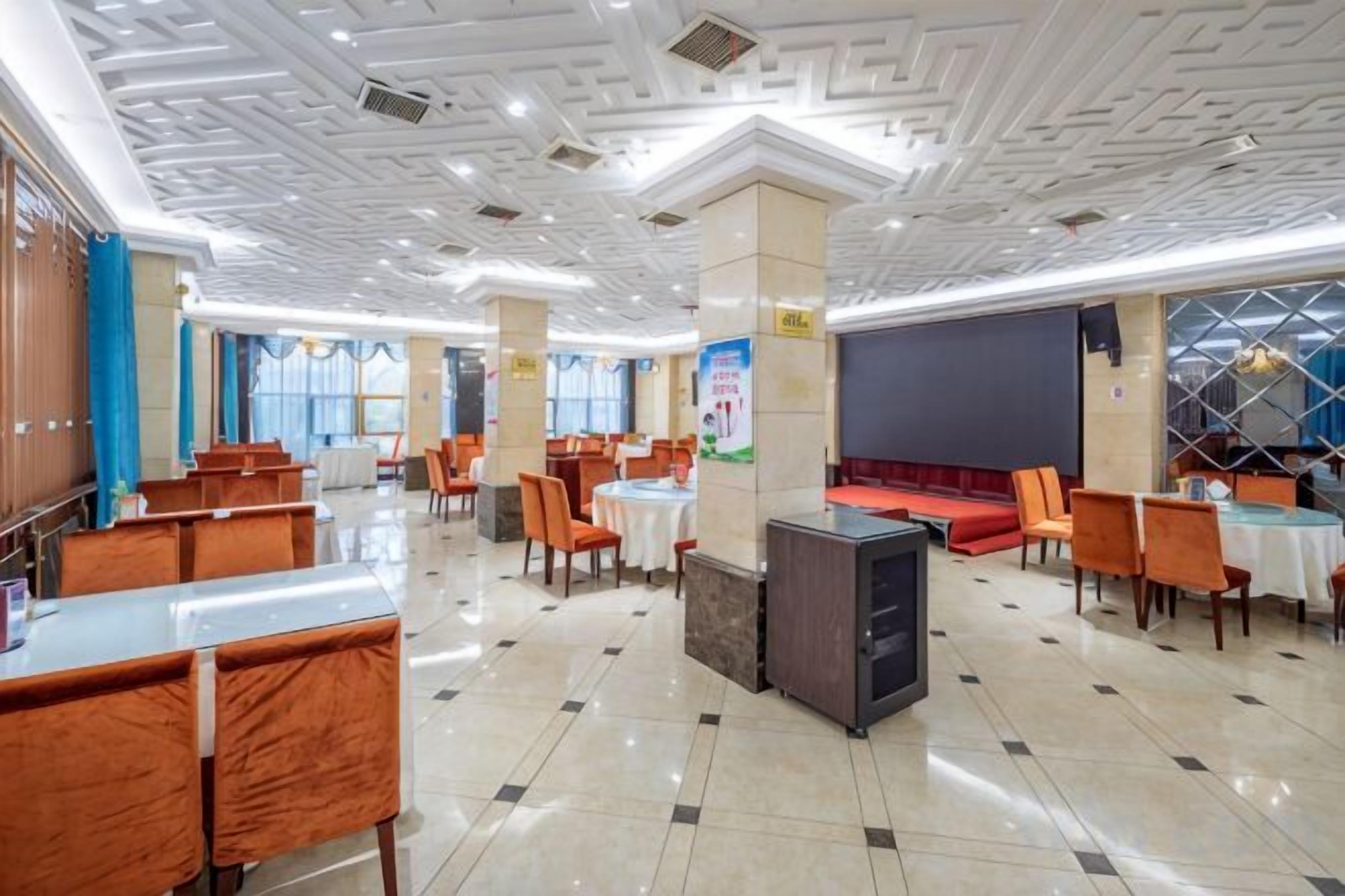 A spacious restaurant with multiple dining areas, a stage, and a modern ceiling design.