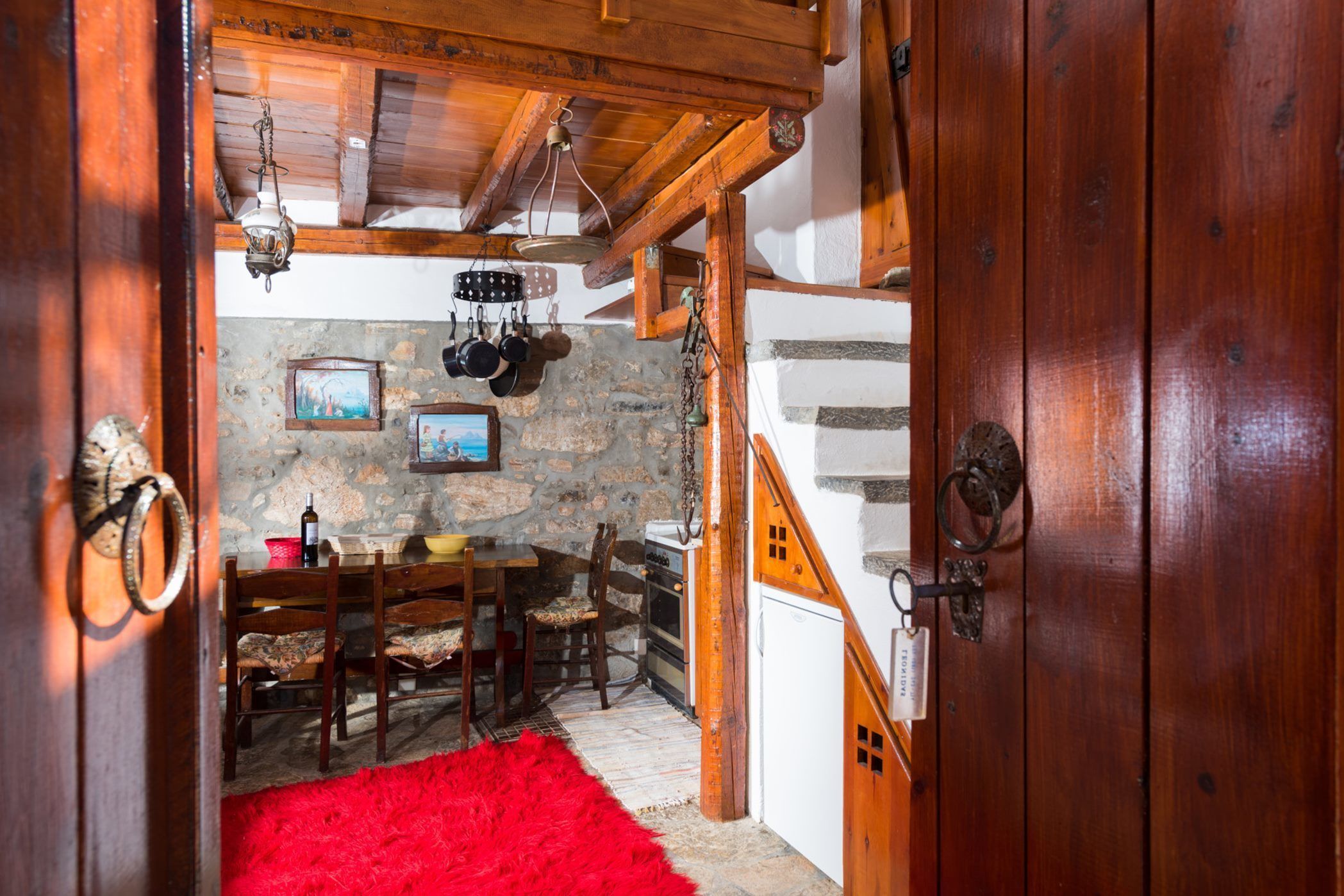 A rustic kitchen with stone walls, wooden beams, and a red rug.