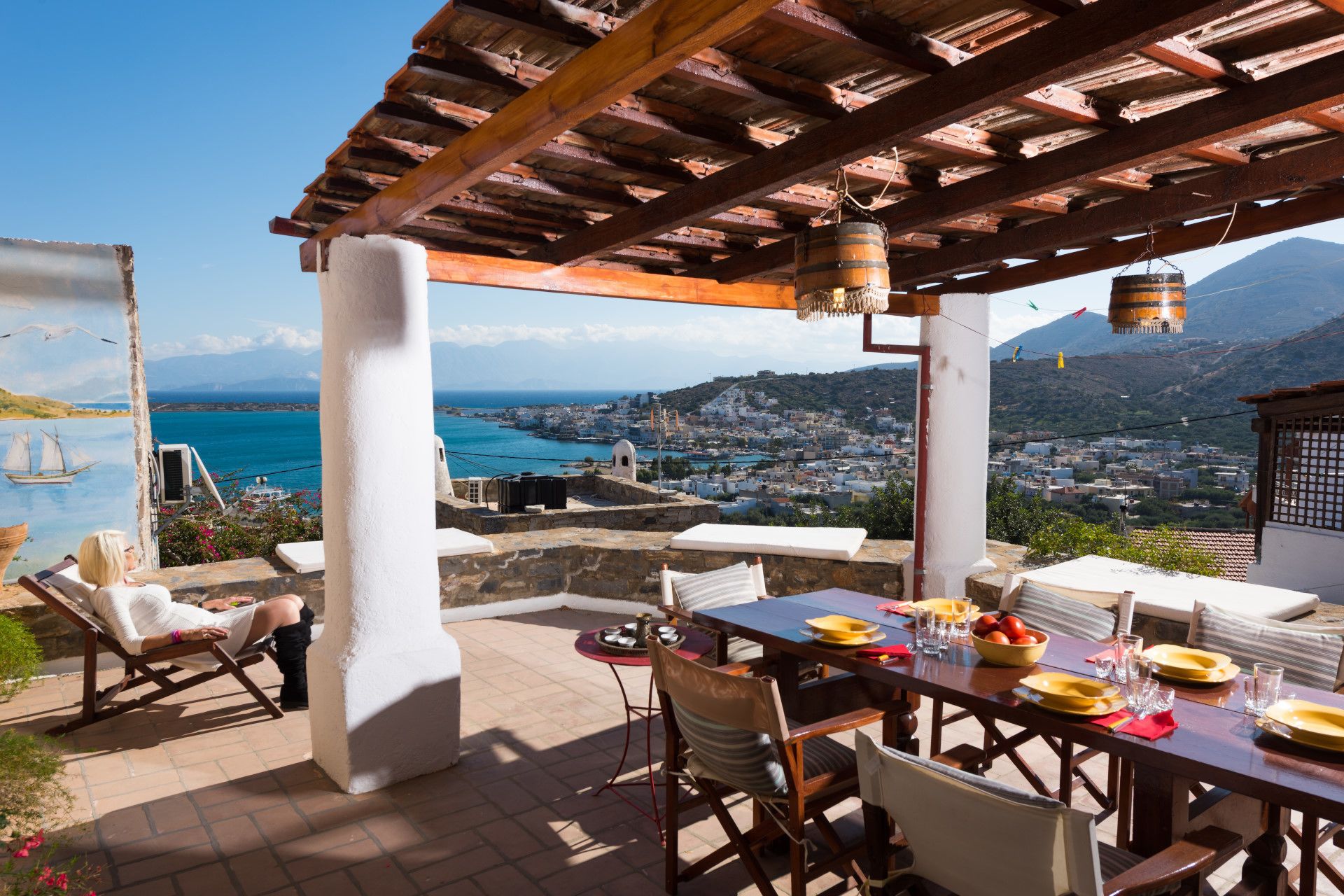A terrace with a table set for dining, overlooking a coastal town and the sea.